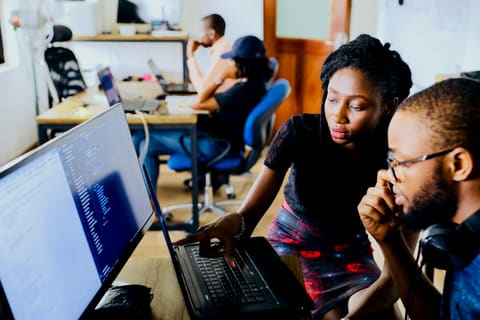 A woman guides a colleague through a task on his computer screen