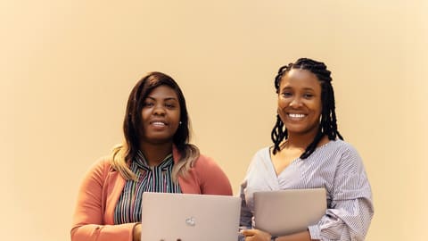 Two smiling professionals holding laptops